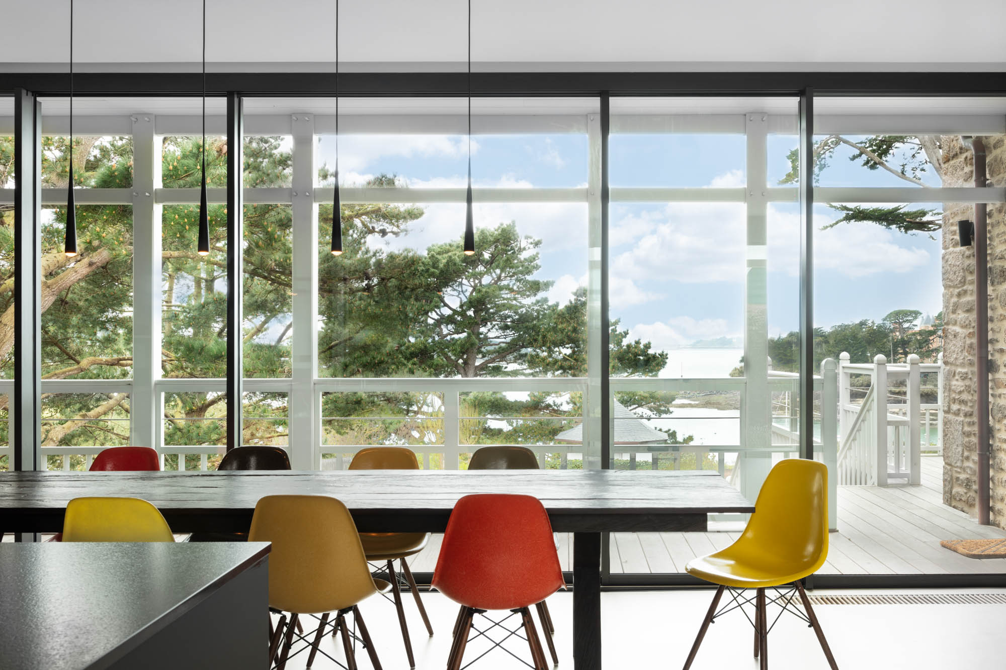 salle à manger aux chaises colorées et baies vitrées donnant sur la mer