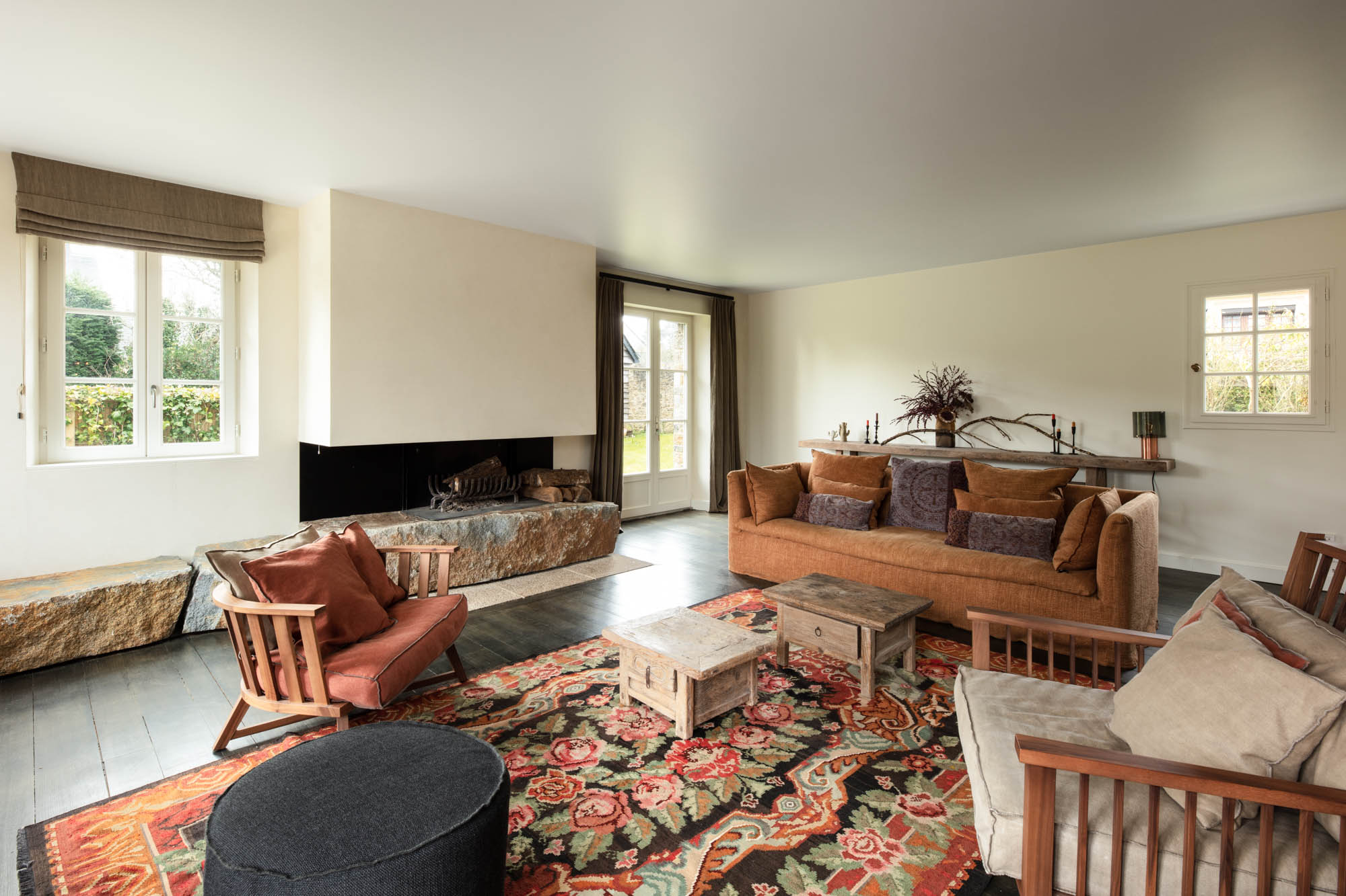 salon avec une cheminée en pierre des tables en bois et des canapés colorés